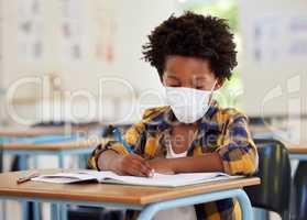 School boy, student and learning while writing and working in his book inside a classroom with a mask due to covid. Young, serious and African child drawing on paper. Smart kid getting an education