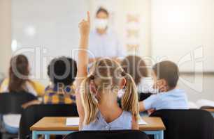 Learning, smart and little girl in class holding up a hand to answer a question at school. Back view of a young student sitting at a classroom desk looking to solve the questions a teacher is asking