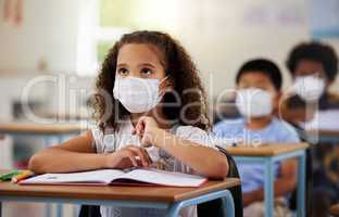 School student with covid learning in class, wearing mask to protect from virus and looking concentrated on education in classroom. Little girl sitting at desk, studying and listening during pandemic