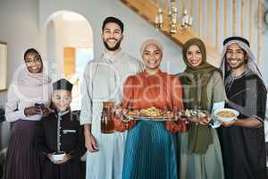 Smiling, festive muslim family celebrating eid or ramadan party lunch together holding dishes of food at home. Happy, traditional islamic religion group of friends enjoying cultural holiday