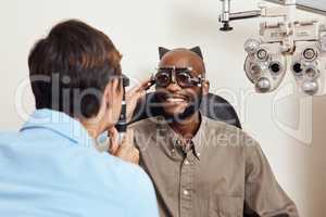 Optical exam, optician or eye doctor at work testing vision or sight of patient at optometrist. Happy, smiling young man checking his eyes for glasses or treatment at an ophthalmologist in a clinic.