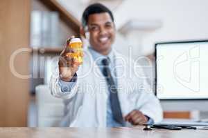 Happy, joyful and friendly male medical doctor offers a bottle of pills to a client with a smile. Smiling, excited and positive healthcare consultant holding antibiotic medicine sitting at desk.