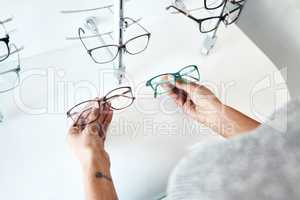 Buying, looking and shopping for glasses at a retail eyewear store and optometrist inside. Customer holding shop stock trying to decide on a new modern style, trendy and stylish frames to buy on sale