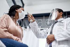 Covid screening with a doctor measuring temperature of a patient using an infrared thermometer during an appointment or checkup. Female getting tested for corona virus and wearing a mask from below