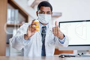 Trustworthy doctor selling good covid medicine or bottle of pills, approving successful medication in hospital. Male healthcare or medical professional wearing mask, showing thumbs up hand gesture.