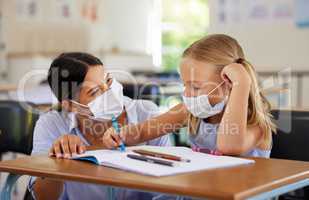 Education, covid and learning with face mask on girl doing school work in classroom, teacher helping student while writing in class. Elementary child wearing protection to stop the spread of a virus