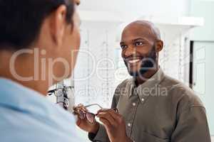 Shopping for glasses at an optician retail store with a smiling man trying to search for a pair. Optometrist and customer service employee selling a happy buying client new and modern spectacles