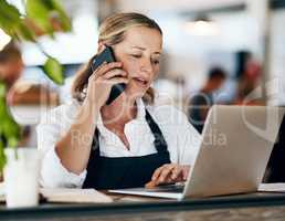Coffee shop owner on a phone call while working online on her laptop inside a local cafe store. Contact us, learn about us and talk to our baristas, managers and small startup business entrepreneurs