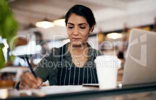 Small business owner working on a budget in her coffee shop and writing a list of stock to order. Serious female entrepreneur developing a growth strategy for her cafe startup