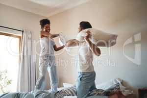 Pillow fight, playing and bonding with a happy couple playing, bonding and spending time together in their bedroom at home. Laughing, having fun and feeling carefree in pyjamas over the weekend