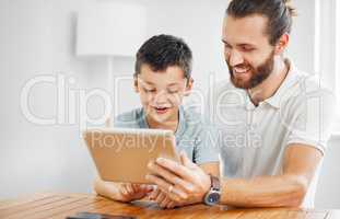 Learning, education and development with a father and son browsing online study material on a tablet at home. Young boy and his dad doing homework or studying with the internet as a resource