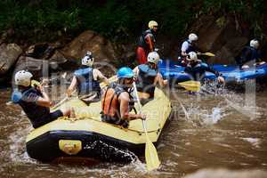 On to our next challenge. a group of cheerful young people in a rubber boat paddling on a river outside during the day.