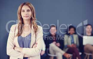 Confidence goes a long way. Cropped portrait of an attractive young businesswoman standing with her arms folded with her colleagues in the background.