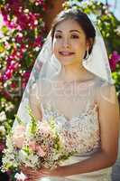 The flowers match her dress. Portrait of a cheerful young bride holding a bouquet of flowers while standing outside during the day.