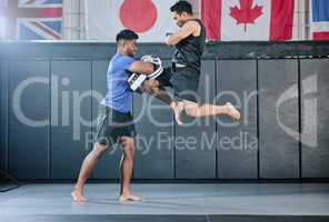 Healthy professional coach sparring and training male kickboxer indoors. Practice sports, exercise and fitness. Two muscular men fighting, jumping and blocking kicks with discipline in class.