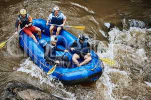 Here comes the next rapid. High angle shot of a group of determined young men on a rubber boat busy paddling on strong river rapids outside during the day.