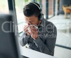 His allergies are flaring up again. a mature man blowing his nose while working on a computer in a call centre.