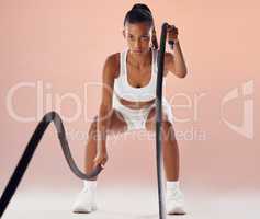 Fit woman doing cardio workout with ropes, exercising for fitness training and looking sporty while posing against a pink studio background. Active and young female athlete doing exercise routine