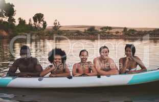 Diverse group of friends having fun while swimming at a lake in summer with a floating kayak boat. Happy, young and multiracial people on vacation enjoying nature and water on a canoe at sunset.