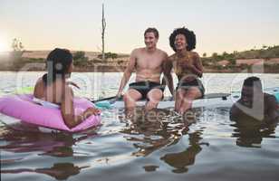 Laughing friends, swimming and playful bonding on summer break with pool inflatable tube in lake, ocean or sea. Diverse group of men or women having fun together and being social on holiday at sunset