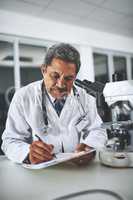 The master of medical science. a mature scientist using a microscope and recording his findings in a laboratory.