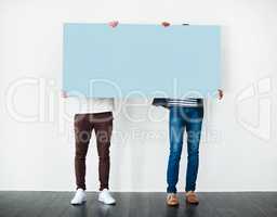 Excuse me, have you seen this. Studio shot of two men covering themselves with a blank placard against a white background.