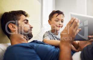 Parenting a media minded little boy. a young man using a digital tablet with his son at home.