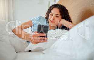 Woman texting, checking messages and holding phone while reading sms and lying awake in her bed in the morning. Happy, content and smiling female playing a game, browsing the internet or social media
