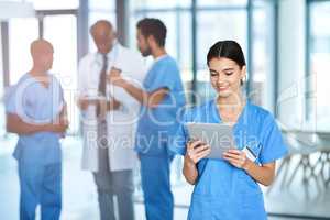 Checking up on her daily medical duties. a young medical practitioner using a digital tablet in a hospital with her colleagues in the background.