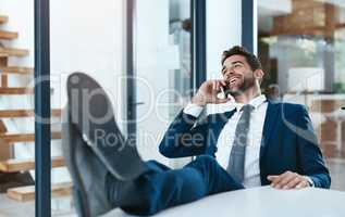 Making millions with one phone call. a handsome young businessman relaxing with his feet up on an office desk while using his phone.