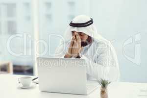 He needs a little divine intervention. a young businessman dressed in Islamic traditional clothing praying while working in his office.