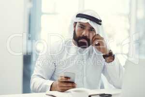 Success would turn this frown upside down. Cropped portrait of a young businessman dressed in Islamic traditional clothing using his cellphone while working in his office.