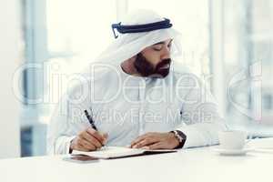 Write it down so you dont forget. a young businessman dressed in Islamic traditional clothing working in his office.