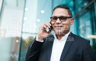 Doing business on the move. Cropped portrait of a handsome mature businessman making a phonecall with his office in the background.