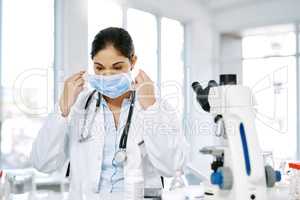 Its time to start a new experiment. a young scientist putting on a surgical mask while working in a lab.