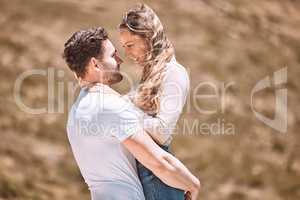 A young loving, affectionate and caring couple bonding while enjoying the day outdoors in nature. Happy, in love and smiling man embracing his wife while holding her outside on a valley or hill