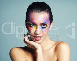 All the colors of the rainbow. Studio shot of an attractive young woman with brightly colored makeup against a blue background.