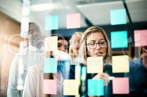 Working together as a group always brings great reward. a group of businesspeople arranging sticky notes on a glass wall in a modern office.