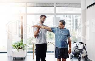 Stretch as far as you can. a young male physiotherapist helping a mature male patient with movement exercises at a clinic.