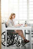 Professional, disabled business woman in wheelchair reading documents, writing or making notes on office desk sitting by laptop. Female entrepreneur with disability doing contract paperwork with pen.