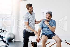 Lets see what the problem is here... a young male physiotherapist helping a mature male patient with movement exercises at a clinic.