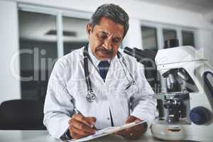 He wont stop until he finds an answer. a mature scientist using a microscope and recording his findings in a laboratory.