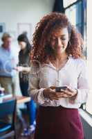 Even smartphones are used to manage business. a young woman using a mobile phone with her team in the background of a modern office.