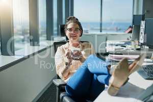 Reach back and relax for a bit. a cheerful young businesswoman drinking coffee while sitting with her feet up on her desk inside of the office.