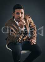 Youll only achieve what you believe. Studio portrait of a handsome young businessman sitting on a chair against a dark background.