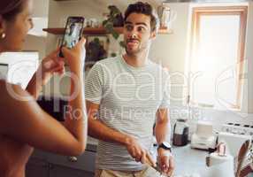 Silly, goofy and interracial couple taking pictures, having fun and cooking together in the kitchen at home. Happy girlfriend taking pictures of boyfriend, making funny faces and preparing dinner