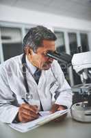 Theres no limit to his medical expertise. a mature scientist using a microscope and recording his findings in a laboratory.