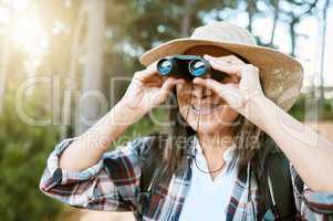Female tourist hiking, looking through binoculars at wild birds in the trees. Happy, carefree and mature woman on nature walk, enjoying the view. Outdoor holiday time to promote health and wellness.