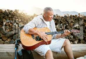 . Mature man, relaxing and playing the guitar while sitting outdoors and enjoying his hobby while getting fresh air. Older man singing a song in his free time in retirement with a musical instrument.