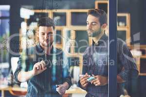 Problem-solving like pros. two young businessmen brainstorming on a glass wall in an office.